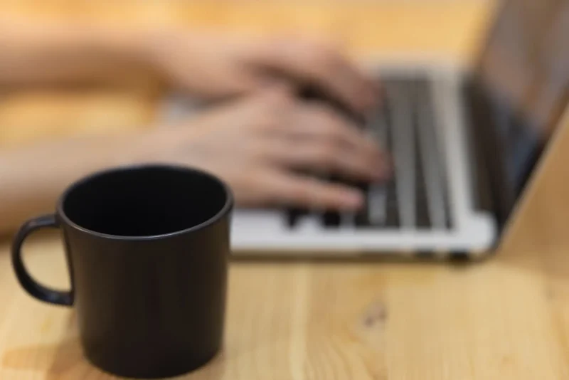 Black cup and hands typing on a laptop.