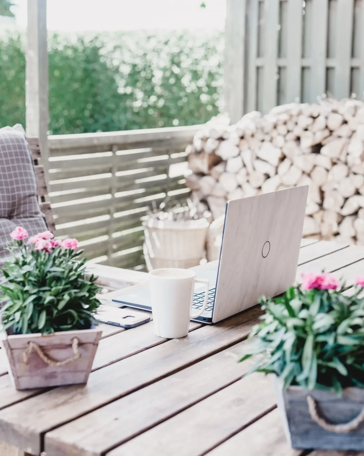 Wooden table with two plants, a cup, and a laptop on it.