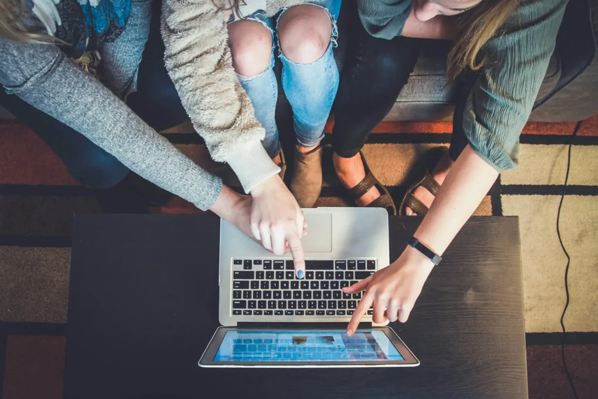 Three people sitting on a couch and using the same laptop.