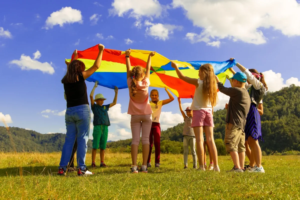 Group of kids playing with a colorful tarp in a field.